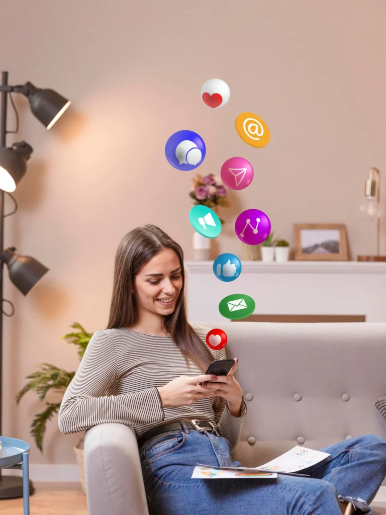 Mulher jovem sentada em um sofá, sorrindo enquanto usa o celular em um ambiente aconchegante de sala de estar. Ícones coloridos de redes sociais e aplicativos flutuam acima do telefone, representando mensagens, curtidas, e-mails e conexões digitais.