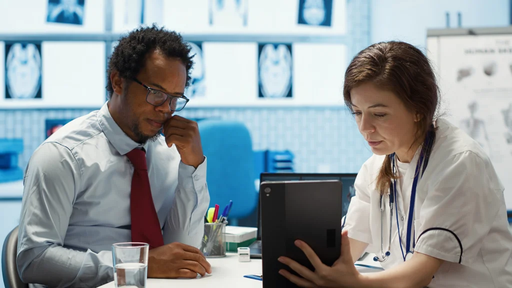 Médico e médica observando exames em um tablet dentro de um consultório moderno.
