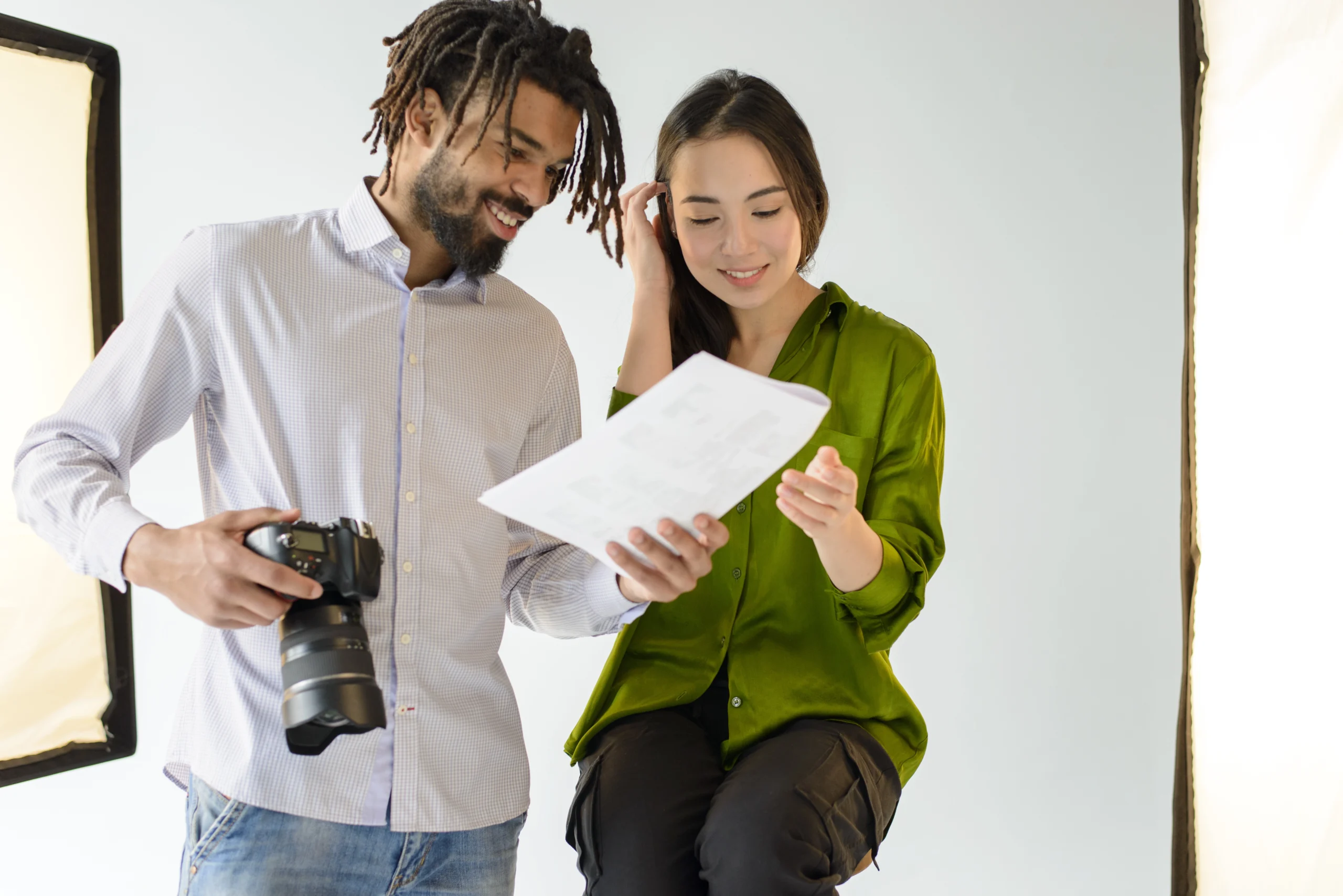 Fotógrafo e colega analisando documentos em um estúdio de fotografia, sorrindo enquanto revisam o material de trabalho.